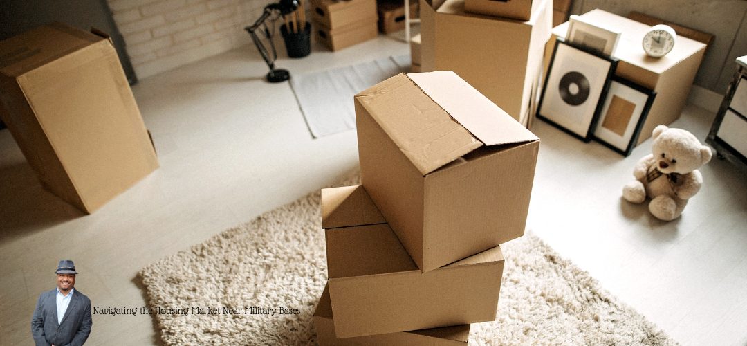 A room filled with stacked cardboard moving boxes, a teddy bear, and framed pictures leaning against the wall. A beige rug covers part of the wooden floor. In the lower-left corner, there is a small image of a man in a suit and hat. The text reads, "Navigating the Housing Market Near Military Bases."