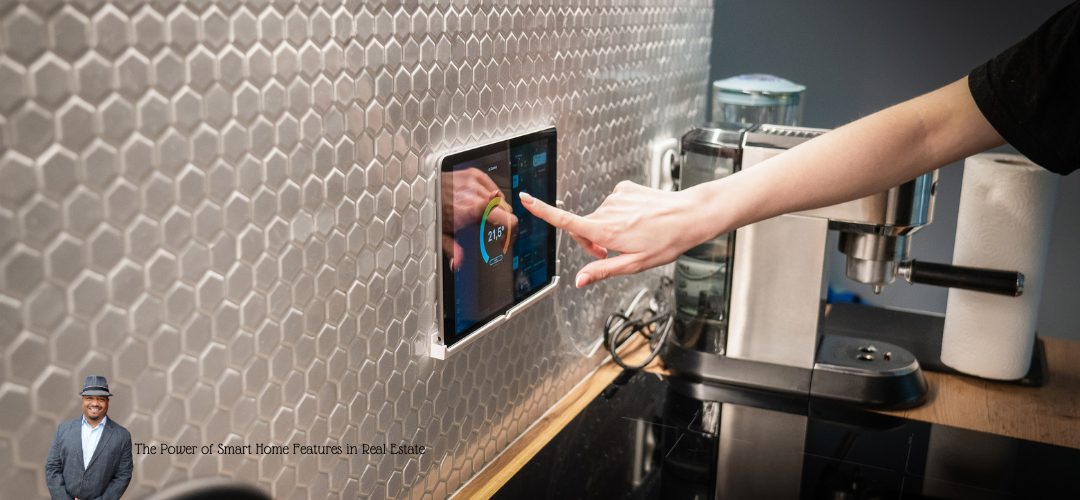 A person interacts with a smart home control panel embedded in a hexagonal-tiled wall in a kitchen. The countertop features a coffee machine and a paper towel roll. Overlay text reads: "The Power of Smart Home Features in Real Estate." A small image of a person in a suit and hat is in the lower left corner.