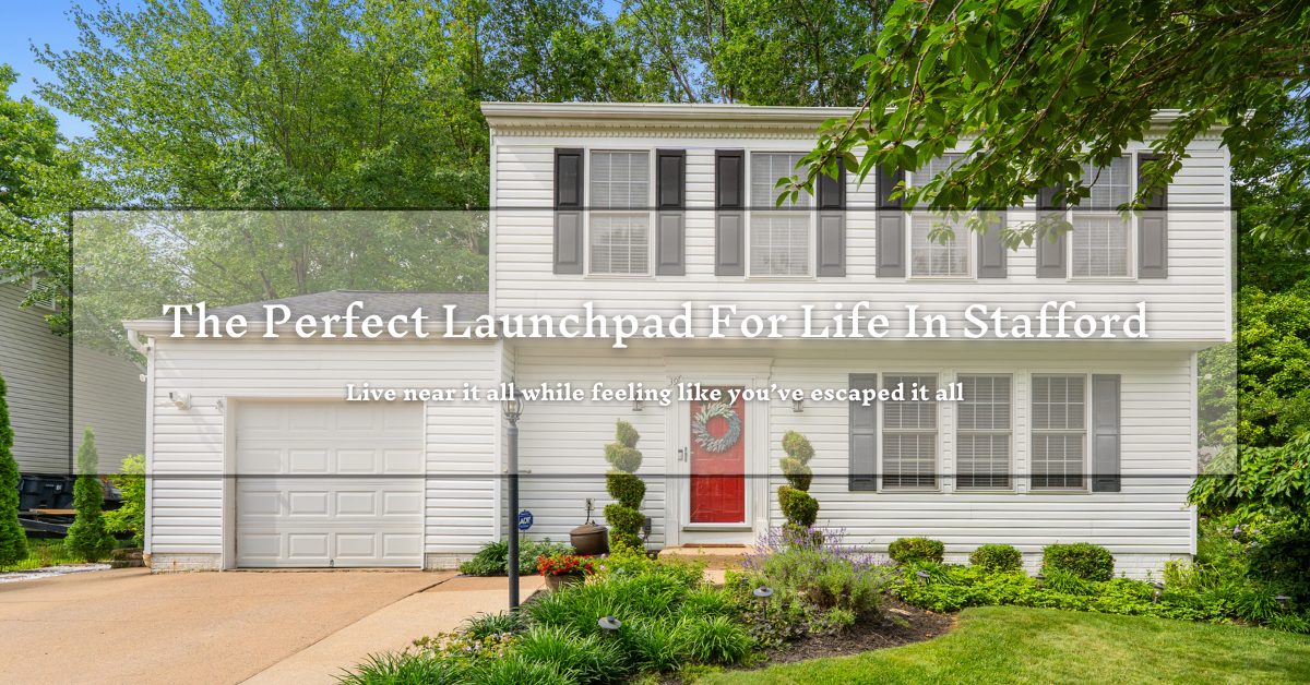 A two-story white house with a red door and several windows, surrounded by greenery and trees. There's a driveway leading to an attached garage. Overlaid text reads, "The Perfect Launchpad For Life In Stafford. Live near it all while feeling like you've escaped it all."