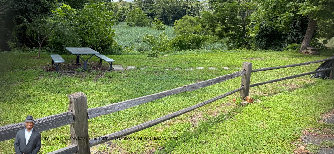 A grassy area with a wooden fence and a picnic table set against a backdrop of lush trees and greenery. In the foreground, there's a person standing near the fence. Overlay text reads: "Two Rare Buildable Lots in the Town of Quantico - What You Need to Know".