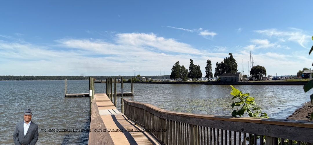 A serene waterfront scene featuring a wooden dock extending into calm water, with trees and a few buildings visible on the opposite shore. A person is visible in the bottom left corner of the image. Overlay text reads: "Two Rare Buildable Lots in the Town of Quantico - What You Need to Know".