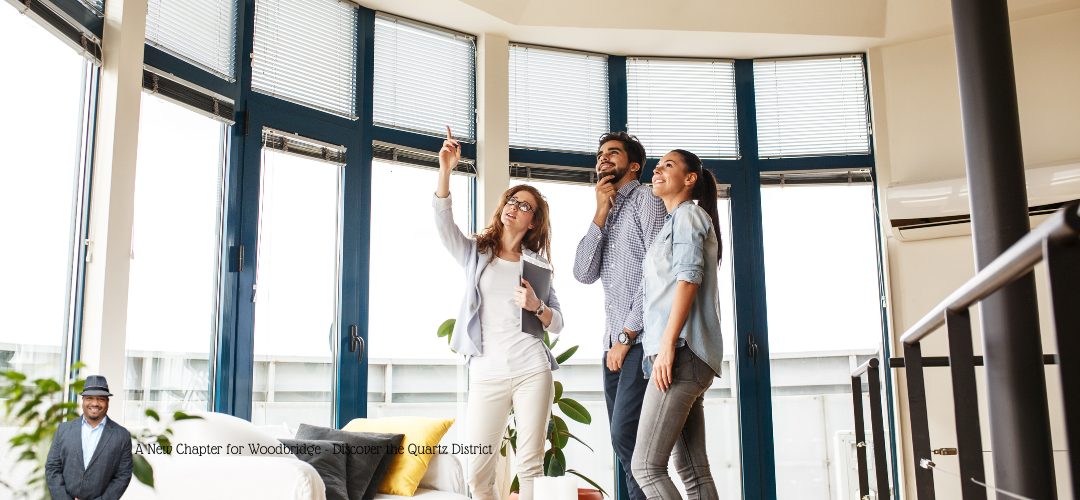 Three people standing in a modern, well-lit room with large windows. One person is gesturing upward, possibly pointing out features of the room to the others. They are smiling and appear interested. The windows allow natural light to fill the space. Text overlay says "A New Chapter for Woodbridge - Discover the Quartz District."
