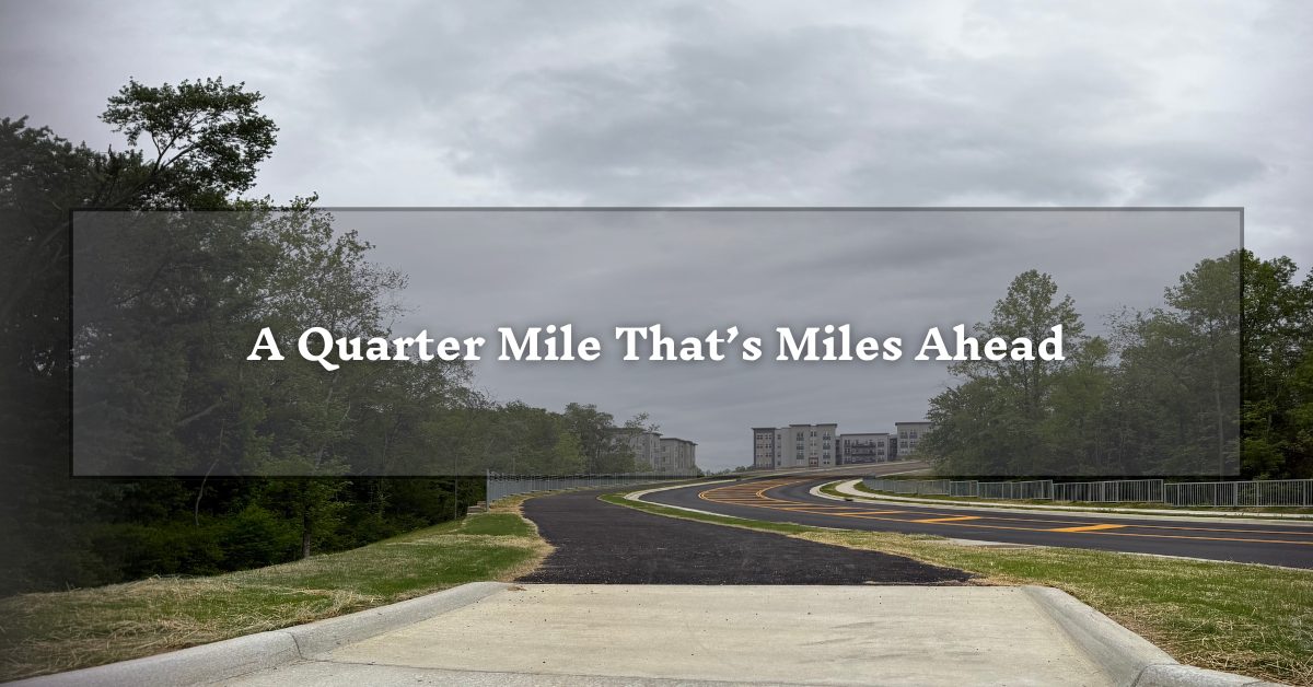 A paved path flanked by trees and a road, with distant residential buildings. A semi-transparent overlay in the center reads, "A Quarter Mile That’s Miles Ahead."