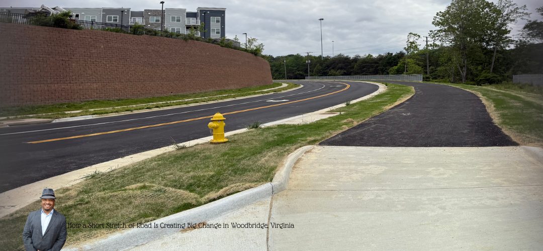 A newly paved road with a yellow fire hydrant on a grassy median, curving into the distance. On the left, residential buildings sit atop a retaining wall. A person in a suit and hat is overlaid at the bottom left corner with text reading, "How a Short Stretch of Road Is Creating Big Change in Woodbridge, Virginia."