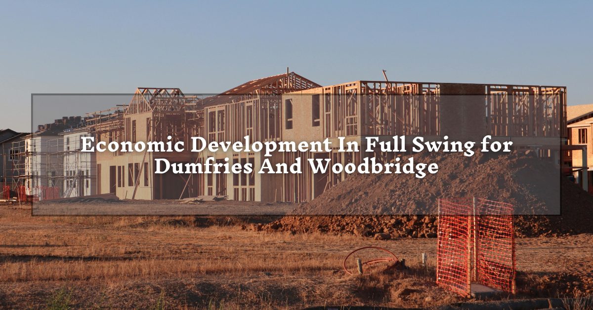 A large building under construction, with a wooden framework and surrounding machinery. The ground is dry and brown, and the sky is dusky. Text over a translucent box reads, "Economic Development In Full Swing for Dumfries And Woodbridge."